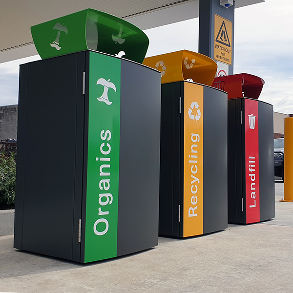 Three waste bins labelled Organics, Recycling, and Landfill in green, yellow, and red, respectively, stand outdoors.