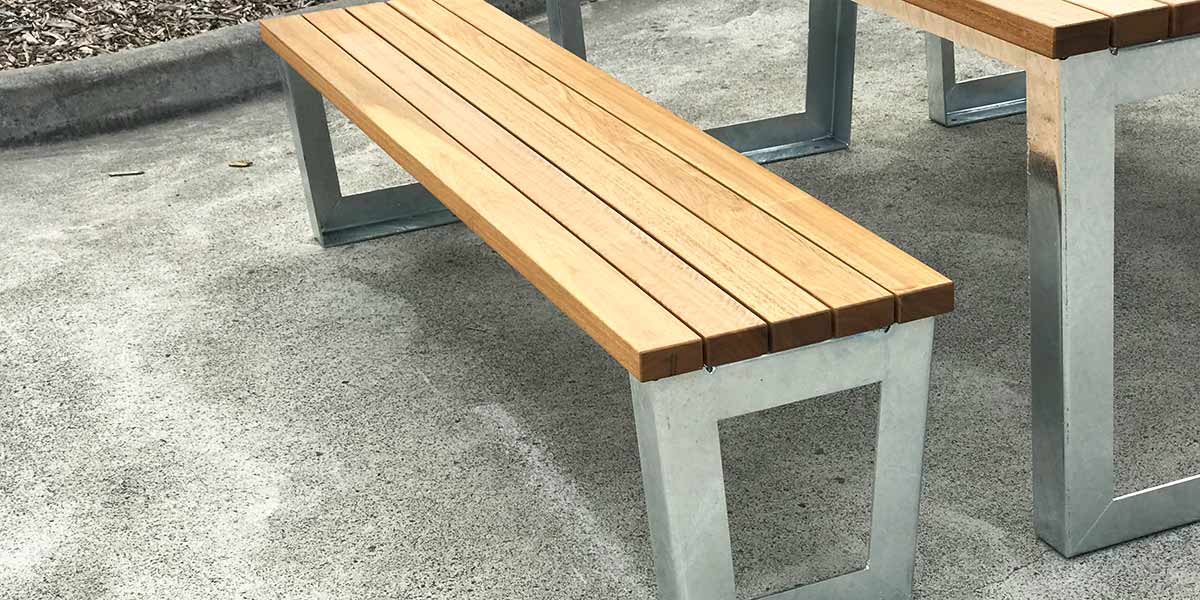 Galvanised metal table and seat frames Wooden bench with metal legs adjacent to a matching table on a concrete surface.