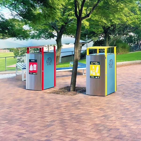 Two bins, one for general waste with a red frame, and another for recyclables with a yellow frame, amidst greenery and benches.