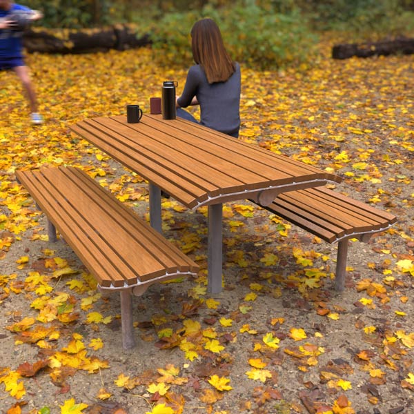 A woman sits at a wooden picnic table in a park. She faces away, with a person playing with a ball in front of her.