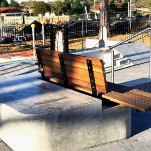 Wooden public bench with a metal frame integrated into a tiered concrete platform in an outdoor space.