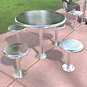 Round metal table with four attached stools with perforated designs. Set on a concrete surface next to a grassy lawn.