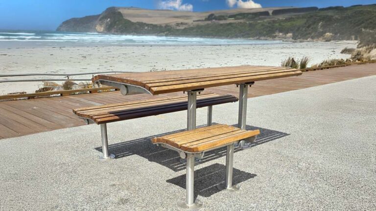 Wooden picnic table with metal legs on a paved seaside path. Picnic table installed by Draffin Street Furniture.