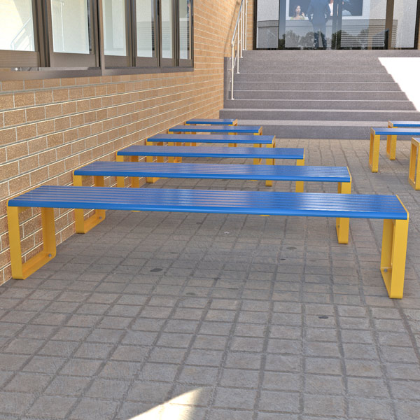 Outdoor area with aluminium benches powder-coated in blue and yellow on a tiled floor beside a brick wall. Stairs in the background.