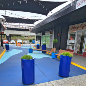 Outdoor shopping area with street furniture like blue planter boxes, bins and wooden benches.