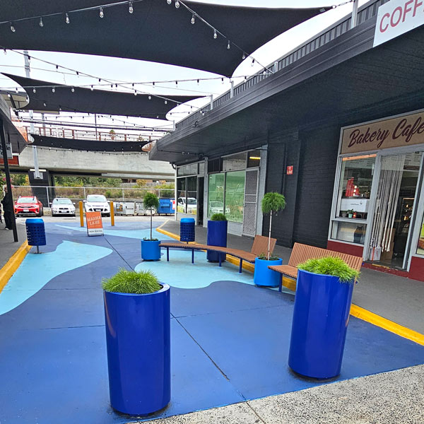 Outdoor shopping area with street furniture like blue planter boxes, bins and wooden benches.