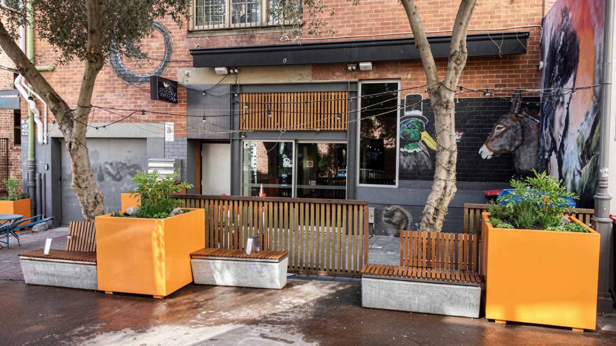 Urban outdoor streetscape with modern wooden seating and planter boxes in bright orange planters.